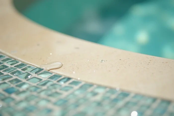 Gros plan sur la surface d'une coque piscine couleur sable beige avec reflets d'eau et mosaïque